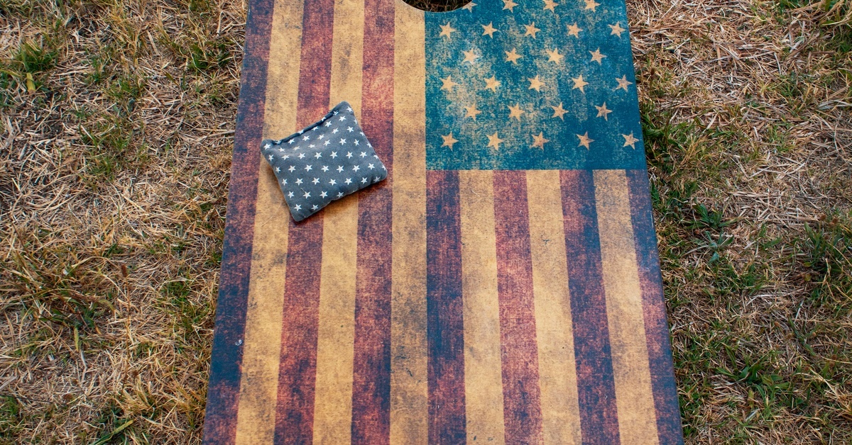 A large North American flag themed cornhole board. the board is worn and a North American flag bean bag sits on it.