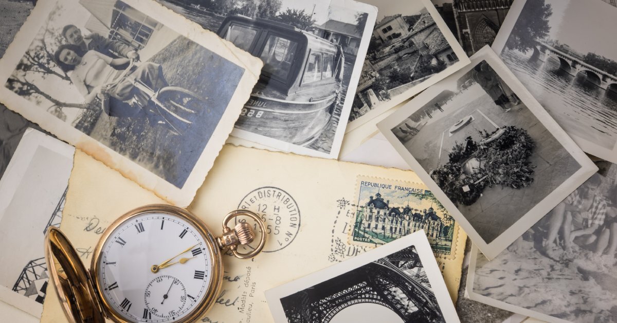 a table with numerous older, black-and-white photographs, a pocket watch, and a postcard with a written note.