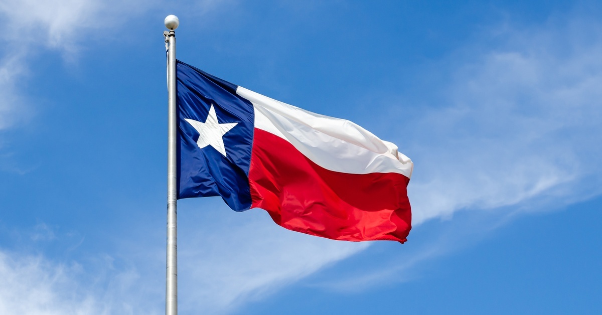 Why US State Flags Make Great Gifts for History Buffs A large flag pole that has the Texas state flag flying high, billowing in the wind. There is a blue sky with clouds in the background.