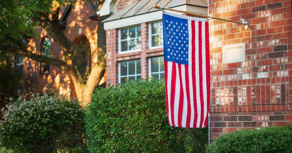 American flag hanging from a wall-mount installed on the outside of a large brick home.
